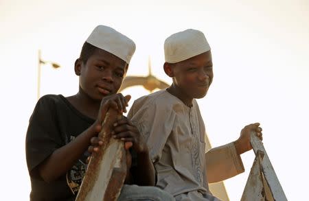 Children sit on wooden scaffolding at dusk in front of the Place de La Nation arch in the Chadian capital N’Djamena October 28, 2014. REUTERS/Emma Farge