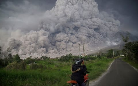 An Indonesian man takes picture of Mount Sinabung volcano as it spews thick volcanic ash into the air in Karo, North Sumatra, on February 19, 2018 - Credit:  ENDRO RUSHARYANTO/AFP
