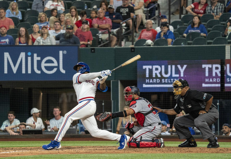 Texas Rangers' Adolis Garcia, left, follows through on a walkoff home run off Washington Nationals relief pitcher Kyle Finnegan as catcher Keibert Ruiz, center, and home plate umpire Laz Diaz, right, look on during the ninth inning of a baseball game Saturday, June 25, 2022, in Arlington, Texas. (AP Photo/Jeffrey McWhorter)