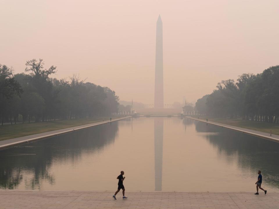 With the Washington Monument in the background and with a thick layer of smoke people run at the National Mall, June 8, 2023, in Washington
