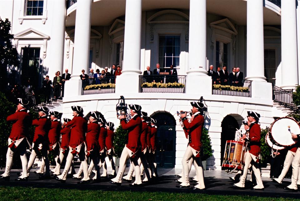 This color photograph shows President Bill Clinton and his guests watching the United States Army Old Guard Fife and Drum Corps during the celebration of the 200th Anniversary of the White House.