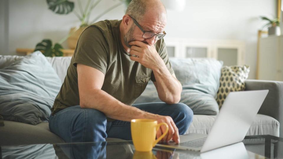 Stressed middle aged man using laptop in living room