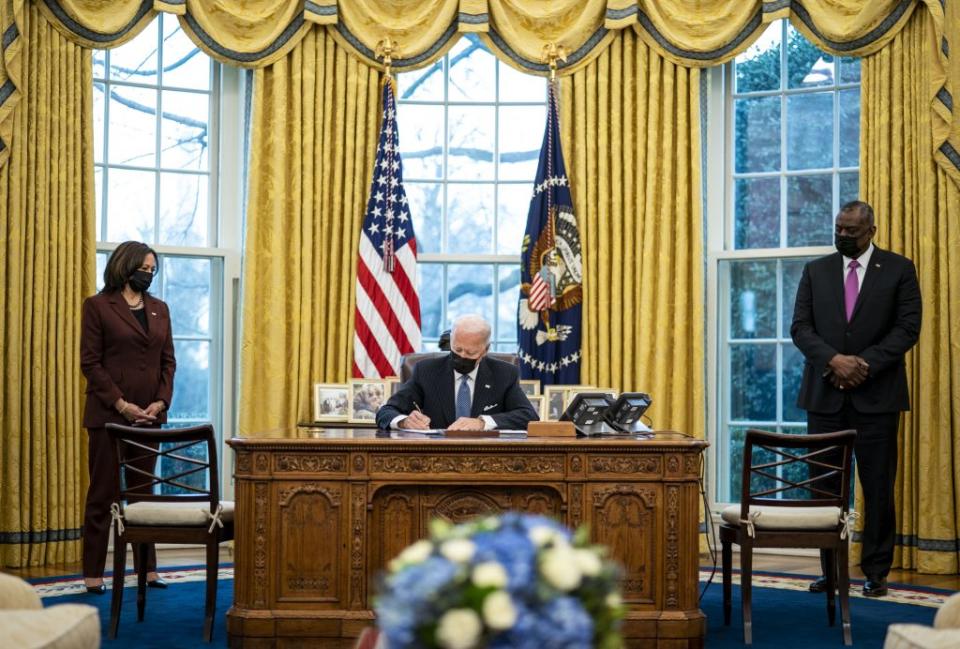 Flanked by Vice President Kamala Harris (L) and Secretary of Defense Lloyd Austin (R), U.S. President Joe Biden signs an executive order in the Oval Office of the White House on January 25, 2021 in Washington, DC. (Photo by Doug Mills-Pool/Getty Images)