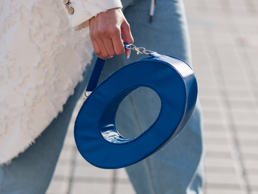 Frau geht eine Straße entlang und trägt eine blaue, donutförmige Handtasche