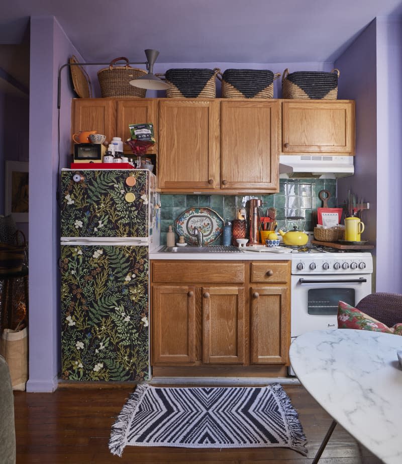 Baskets above cabinets in purple painted kitchen with green backsplash.