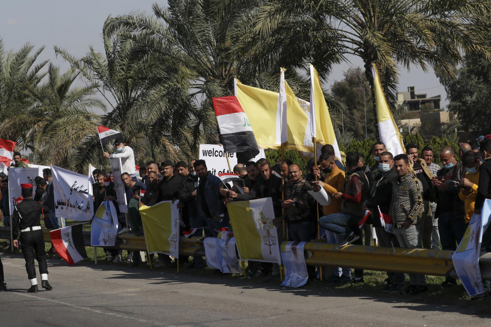 People stand by the road as they wait for Pope Francis, in Baghdad Iraq, Friday, March 5, 2021. Pope Francis heads to Iraq on Friday to urge the country's dwindling number of Christians to stay put and help rebuild the country after years of war and persecution, brushing aside the coronavirus pandemic and security concerns. (AP Photo/Andrew Medichini)