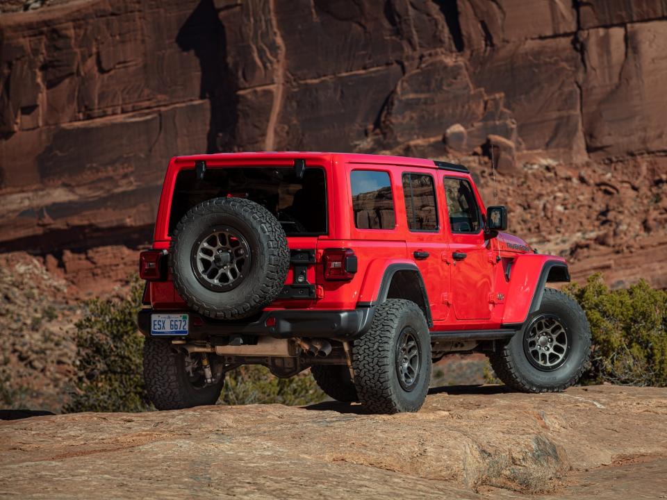 A red Jeep drives off-road in a sandy desert area.