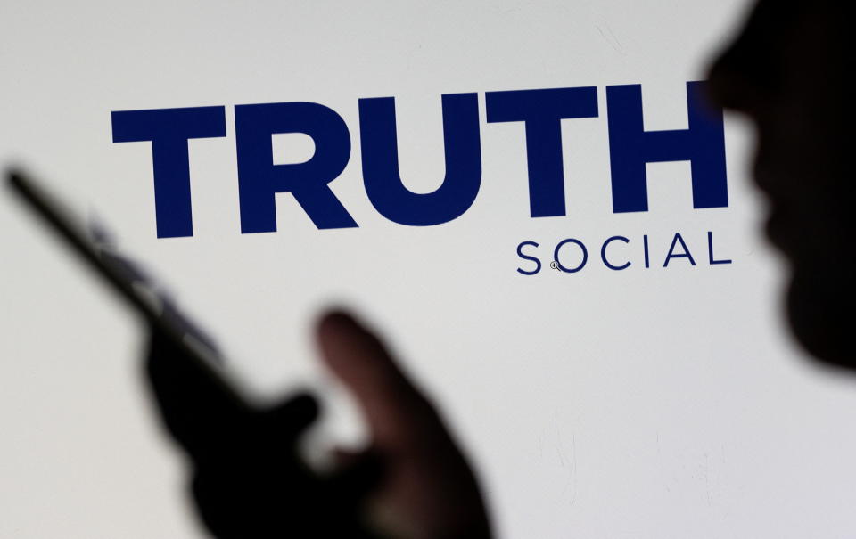 The Truth social network logo is seen displayed behind a woman holding a smartphone in this picture illustration taken February 21, 2022. REUTERS/Dado Ruvic/Illustration