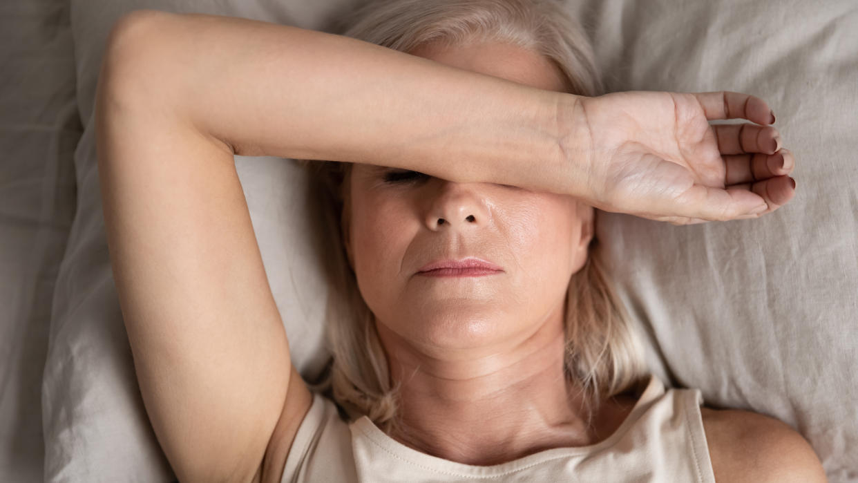 Close up top view middle-aged woman lying down in bed on pillow put hand on face, concept of female having insomnia sleeping disorder or migraine pain, melancholic mood, personal life troubles concept