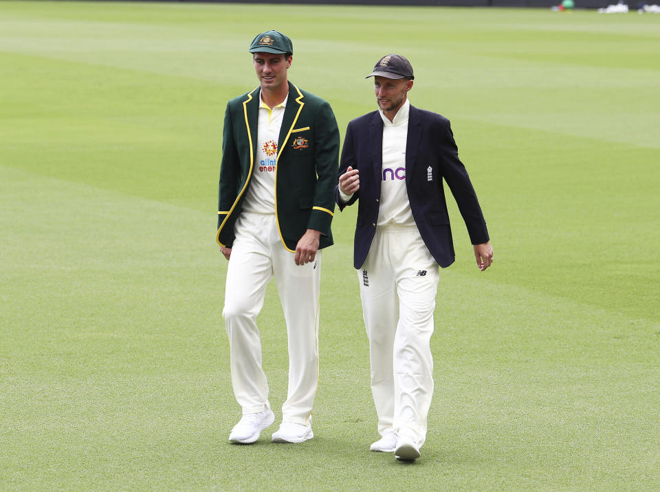 Australian captain Pat Cummins, left, and England captain Joe Root walk across the field after posing with the Ashes trophy at the Gabba cricket ground ahead of the first Ashes cricket test in Brisbane, Australia, Sunday, Dec. 5, 2021. (AP Photo/Tertius Pickard)