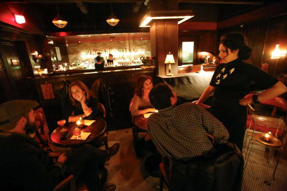 A server chatting with people sitting at a dinner table inside a dimly-lit speakeasy.
