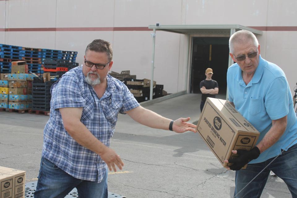 Lyn Poplin, Associate Pastor of Greenwood United Methodist Church, hands a box of drinking water to David Webb, volunteer, at the River Valley Regional Food Bank Wednesday, June 15 in Fort Smith.