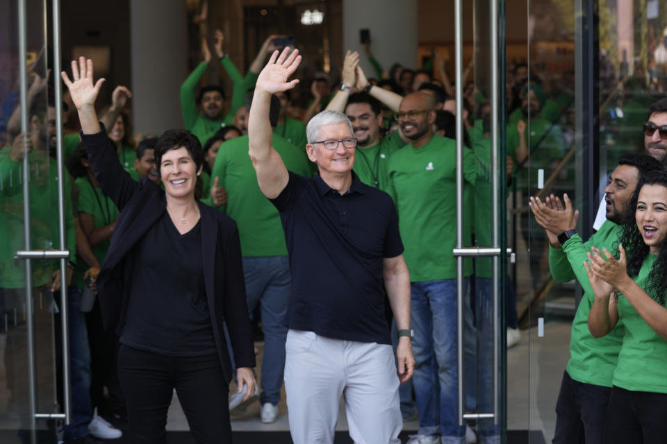 Apple CEO Tim Cook, center, with Senior Vice president of retail Deirdre O'Brien wave to the dozens of people waiting outside during the grand opening Apple Inc. first flagship store in Mumbai, India, Tuesday, April 18, 2023. Apple Inc. is set to open its first flagship store in India in a much-anticipated launch Tuesday that highlights the company's growing aspirations to expand in the country it also hopes to turn into a potential manufacturing hub. (AP Photo/Rafiq Maqbool)