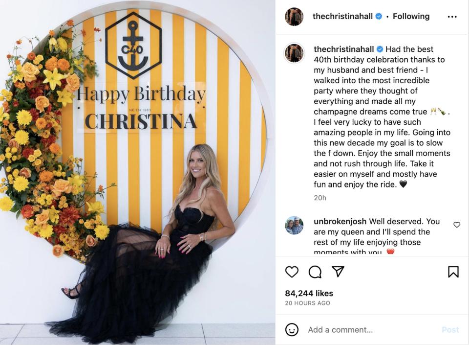 A screenshot of Christina Hall's Instagram post. She poses in a black dress in front of a photo booth with yellow and white stripes and a floral arch.