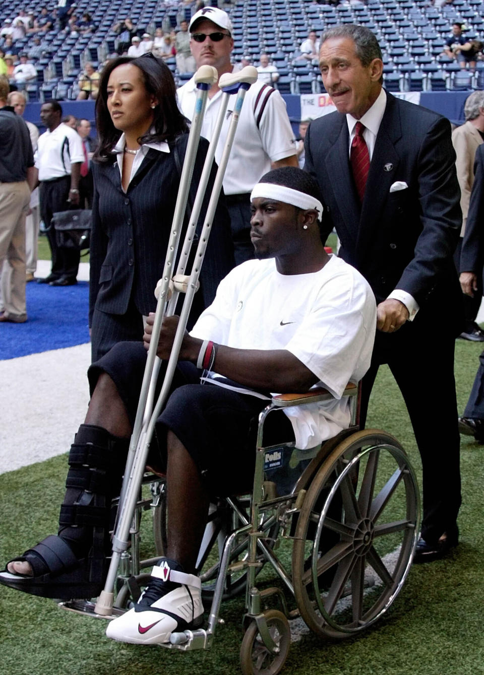 FILE - Atlanta Falcons quarterback Michael Vick is pushed by team owner Arthur Blank, right, as the team's vice president of communications and community affairs, Susan Bass, left, walks with them on the sideline before the team's NFL football game against the Dallas Cowboys in Irving, Texas, Sept. 7, 2003. The Falcons started 2-10 behind Doug Johnson and Kurt Kittner before Vick returned. (AP Photo/Donna McWilliam, File)