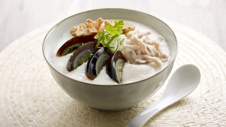white placemat bowl and spoon with congee chicken and sliced century egg