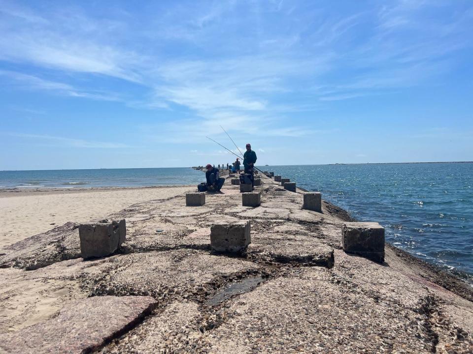 men fishing on the rocks above the ocean at isla blanca park on south padre island