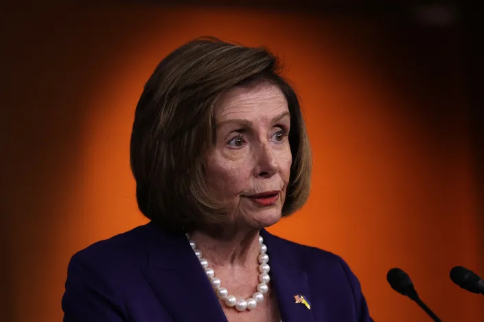 House Speaker Nancy Pelosi, wearing a thick pearl necklace, at a microphone.