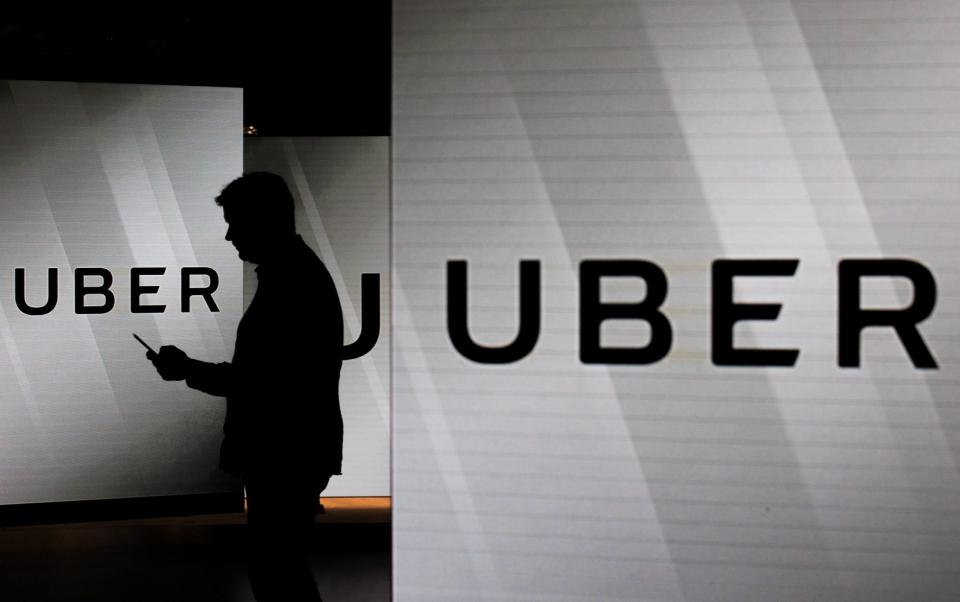 A man checks his smartphone while standing amongst illuminated screens bearing the Uber logo