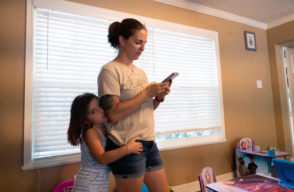Erin Ruiz looks at photos on her phone from her time with Austin-Travis County EMS while her 4-year-old daughter, Mackenzie, hugs her at their home in Waco.