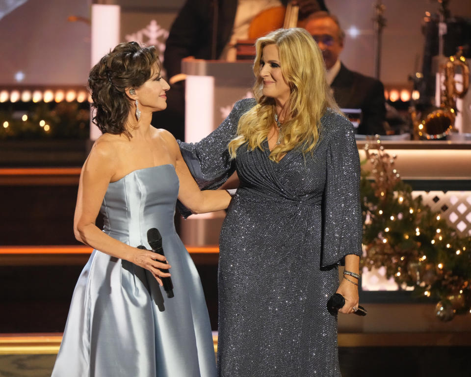 Amy Grant in a silver strapless dress next to Trisha Yearwood who's wearing a gray sparkly dress with long sleeves.