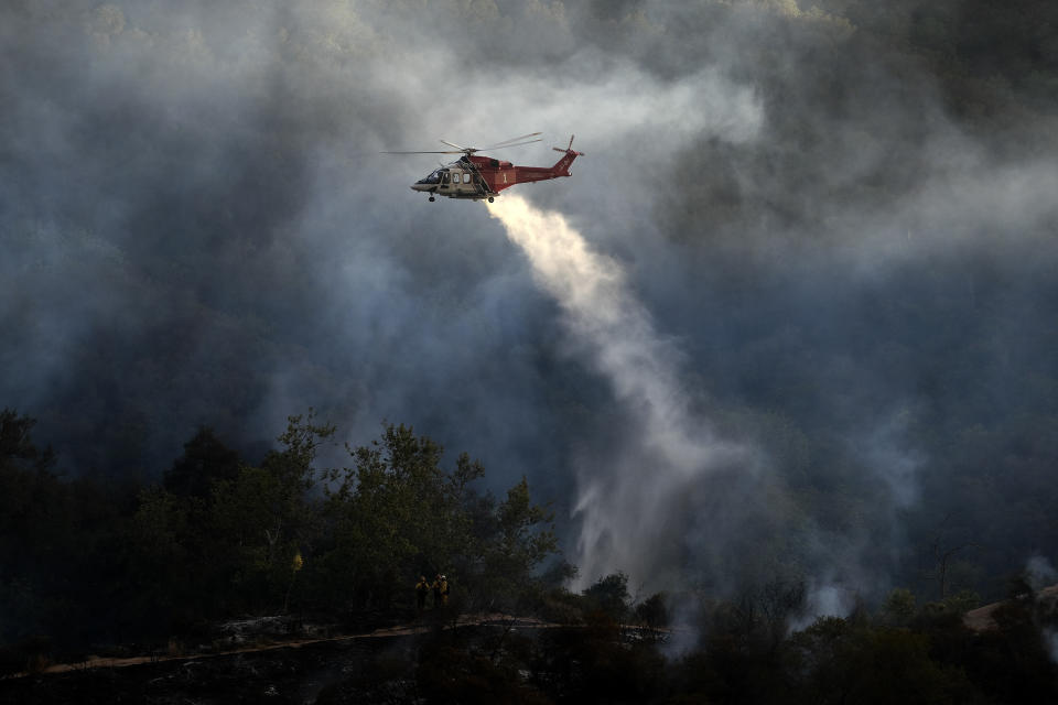 A firefighting helicopter drops water onto a brush fire scorching at least 100 acres in the Pacific Palisades area of Los Angeles on Saturday, May 15, 2021. (AP Photo/Ringo H.W. Chiu)