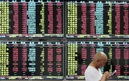 An investor looks at his mobile phone in front of electronic screens showing stock information at a brokerage house in Jiujiang, Jiangxi province, China, August 10, 2015. REUTERS/Stringer