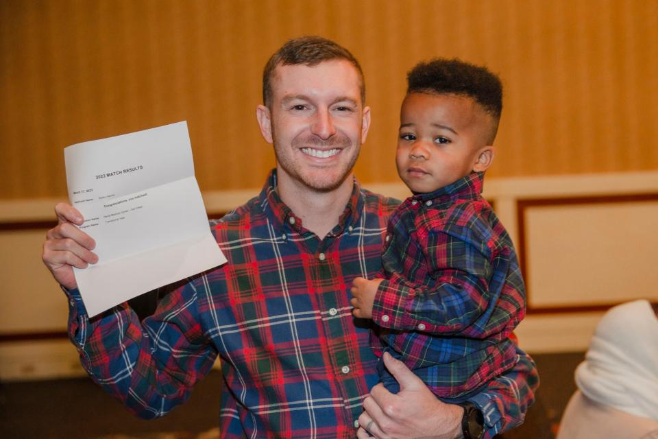 Bailey Harvey displaying his Match Day results while holding his son. Harvey, a military student of the United States Navy will complete his radiology residency at the Naval Medical Center in San Diego, California.