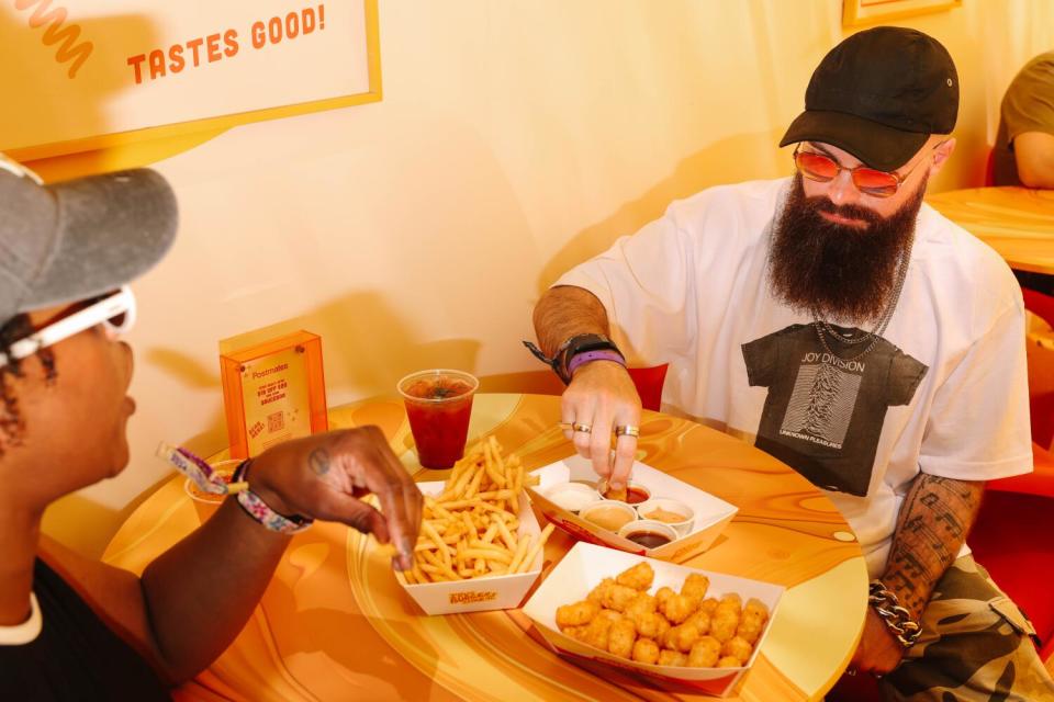 Two people eat tots and dipping sauce together at a table