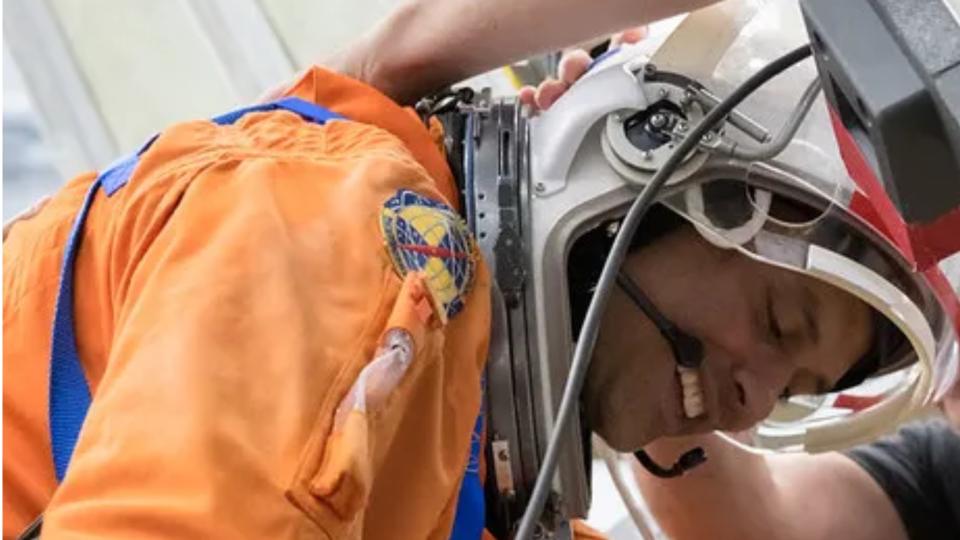 Ένας αστροναύτης σκύβει μπροστά φορώντας διαστημική στολή και κράνος