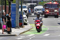 A delivery driver on a scooter keeps pace with a fire engine on a call in the Seaport District, Friday, June 7, 2024, in Boston. A soaring demand for food delivered fast has spawned small armies of couriers in a growing number of cities where delivery scooters, motorcycles and mopeds zip in and out of traffic and hop onto sidewalks alongside startled pedestrians racing to drop off salads and sandwiches. (AP Photo/Charles Krupa)