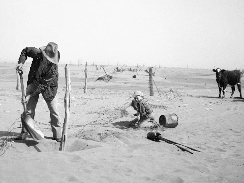 A farmer raises his fence to stop it being buried in sand in Oklahoma in 1936.