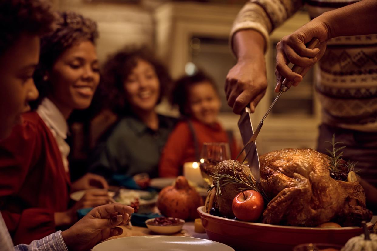 Close up of African American man carving Thanksgiving turkey during family meal at dining table.