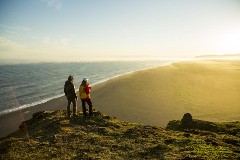 A couple stand on a cliff overlooking the ocean.