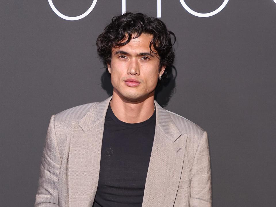 charles melton in a black tshirt and grey suit on a red carpet