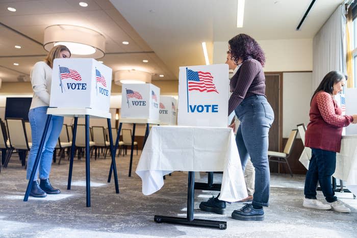 Three people at voting booths with privacy screens marked "VOTE"