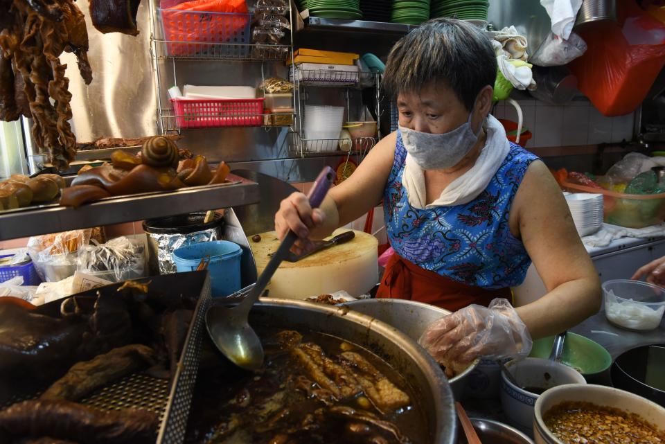 This photo taken on April 21, 2020 shows Lim Bee Hong ladling a broth of spices and herbs as she prepares food at her small food stall, as the business has moved to delivery only due to the COVID-19 coronavirus outbreak in Singapore. - From Facebook groups to hyper-local delivery services, Southeast Asia's street food chefs are cooking up creative ways to sell their wares as they struggle to survive amid the coronavirus pandemic. (Photo by Catherine LAI / AFP) (Photo by CATHERINE LAI/AFP via Getty Images)