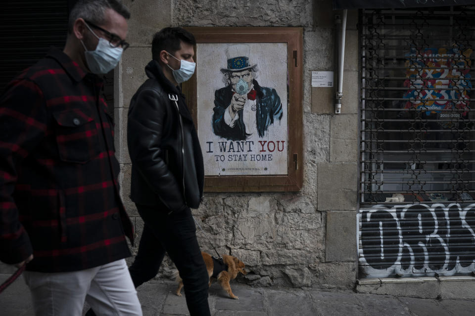 People walk past a poster that reads 'I want you to stay home', by artist TvBoy amid a lockdown in Barcelona, Spain, Tuesday, March 24, 2020. More than 1.5 billion around the world have been told to stay in their homes. For most people, the new coronavirus causes only mild or moderate symptoms. For some it can cause a more serious illness. (AP Photo/Felipe Dana)