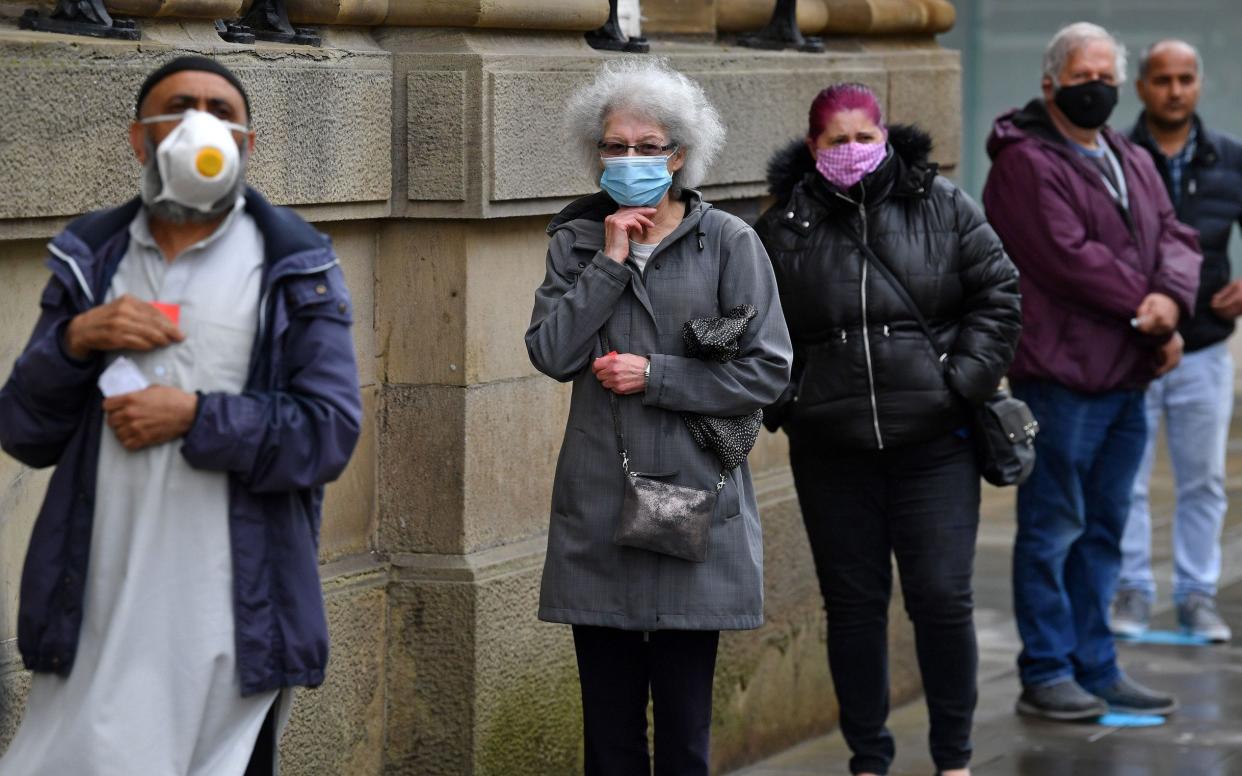 Customers, wearing a face mask or covering due to the COVID-19 pandemic, socially distance as they queue to enter a NatWest bank in Blackburn - AFP