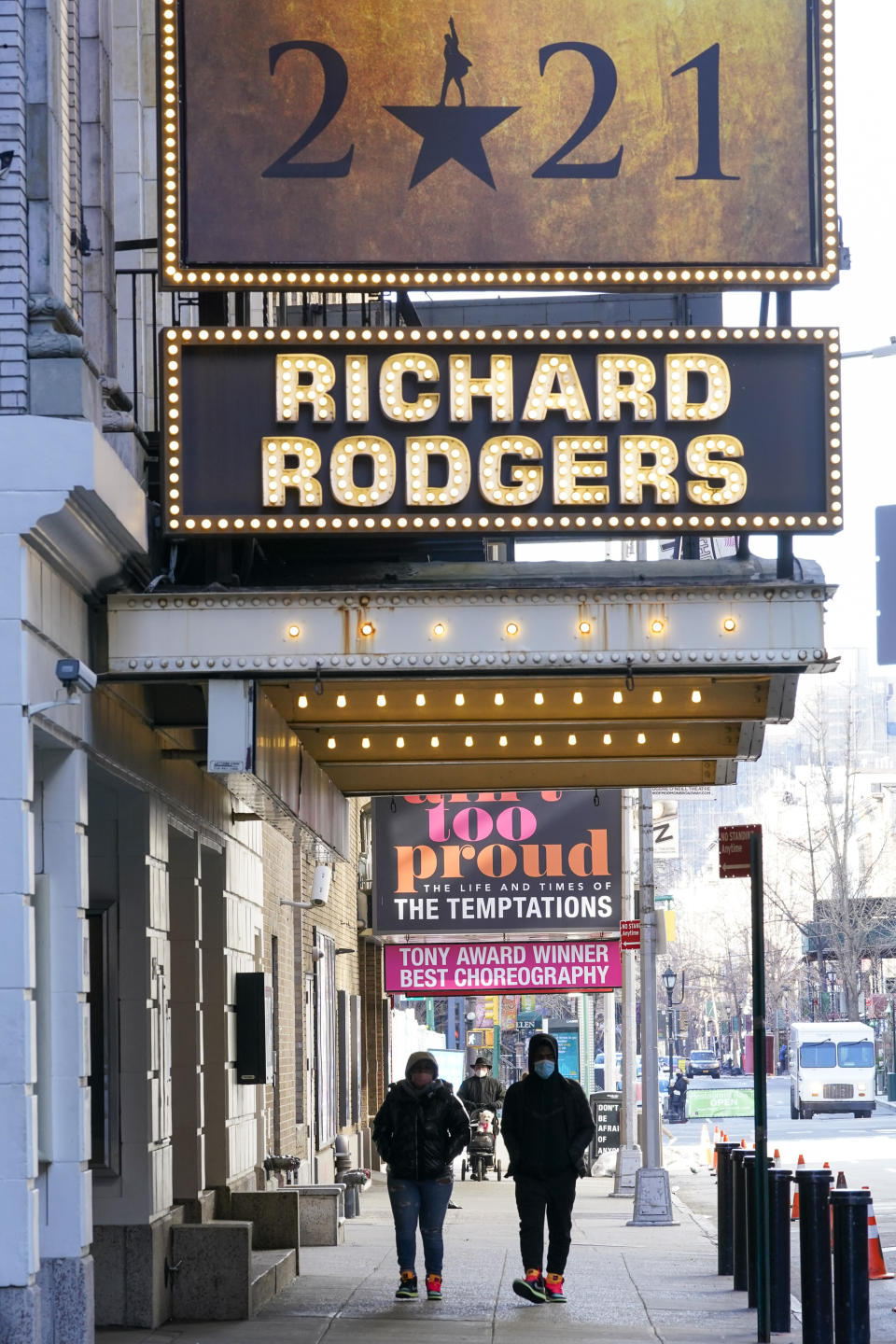 Pedestrians walk past closed Theatres, Sunday, Jan. 10, 2021, in the Hell's Kitchen neighborhood of New York. The boarded-up windows and For Rent signs are all over the place in Manhattan’s Hell’s Kitchen neighborhood. Nearby, the Broadway theaters are all dark. But the economic darkness brought on by the coronavirus pandemic has had a few bright spots. A couple of well-loved venues have gotten financial boosts, thanks to online fundraising campaigns and even a telethon. (AP Photo/Mary Altaffer)