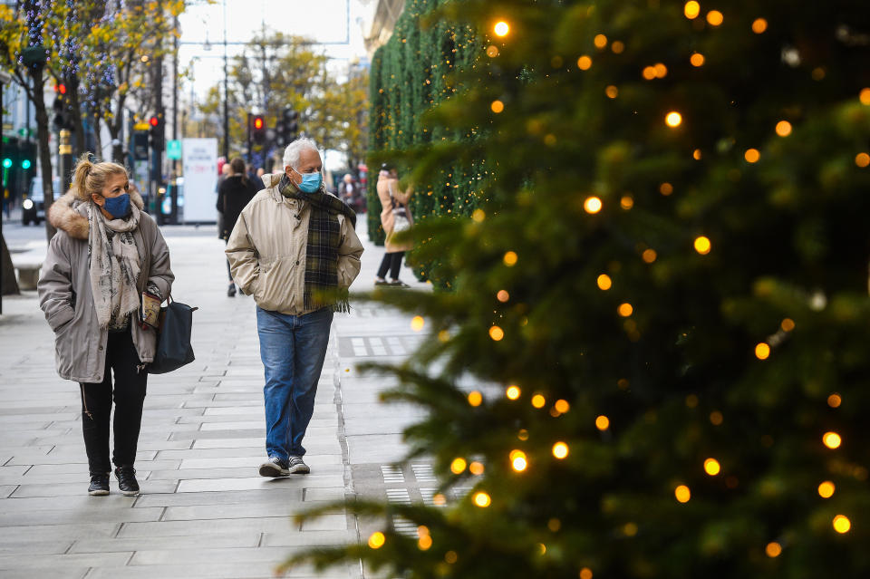 People wearing face masks pass Christmas lights outside shops on Oxford Street, London, as England continues a four week national lockdown to curb the spread of coronavirus.