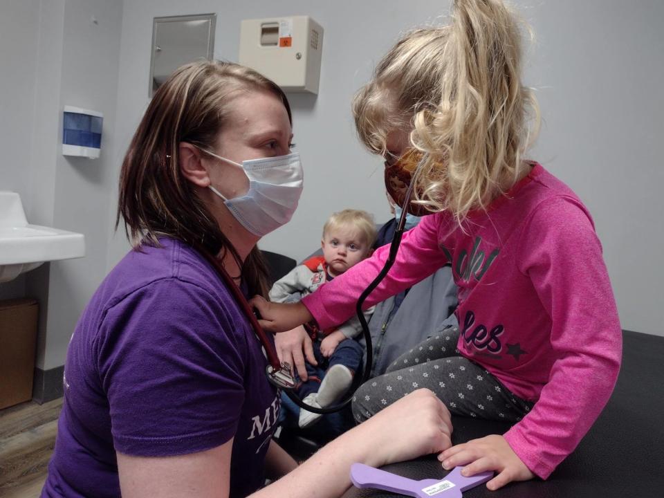 little girl in moderna vaccine trial, holding nurse's stethoscope