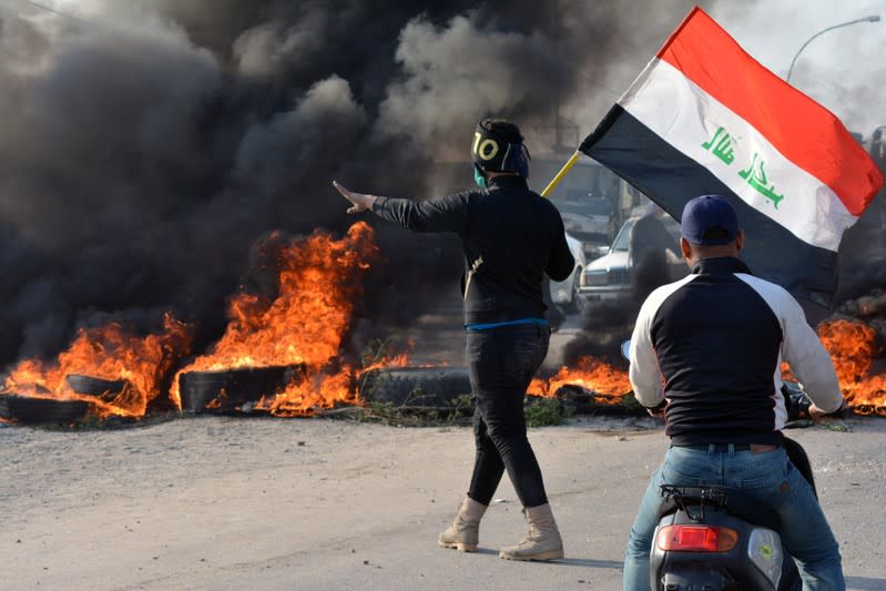 A demonstrator holds an Iraqi flag near burning tires during ongoing anti-government protests in Nassiriya