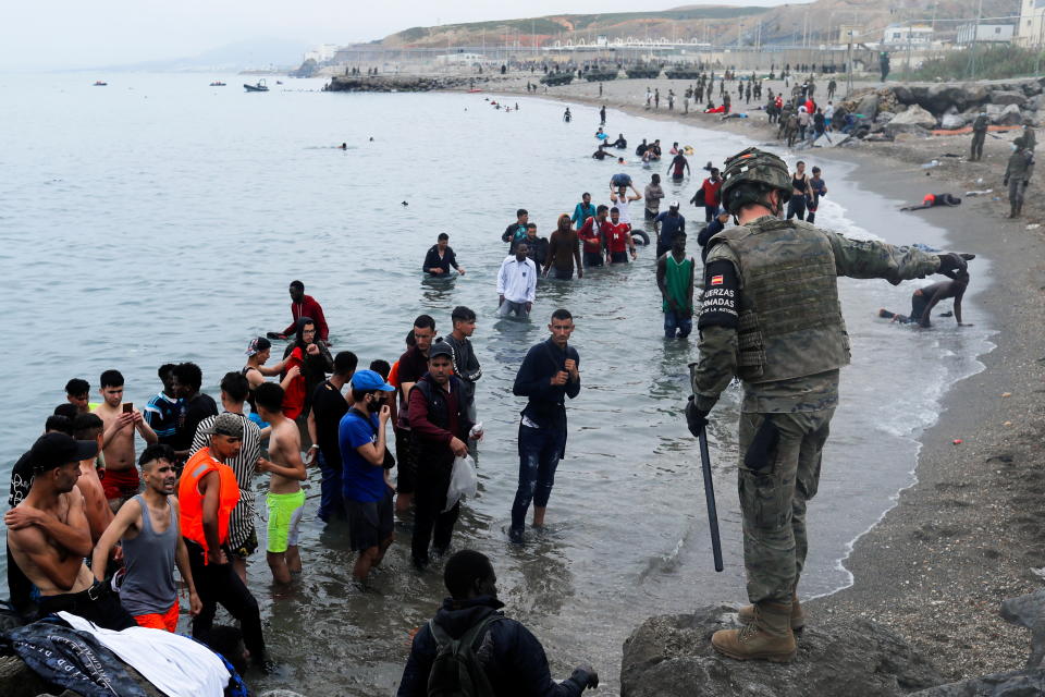 A Spanish legionnaire indicates the direction to follow to Moroccan citizens on El Tarajal beach, as they get out of the water on the Spanish side of the fence between the Spanish-Moroccan border, after thousands of Moroccans swam across this border on Monday, in Ceuta, Spain, May 18, 2021. REUTERS/Jon Nazca