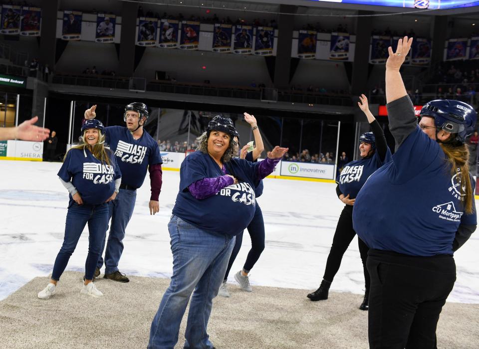 Local teachers wave to the crowd while holding piles of money in their shirts on Saturday, December 11, 2021, in the first-ever Dash For Cash between periods at the Sioux Falls Stampede game. The teachers can use the money collected during the event for classroom programs and enhancements. 