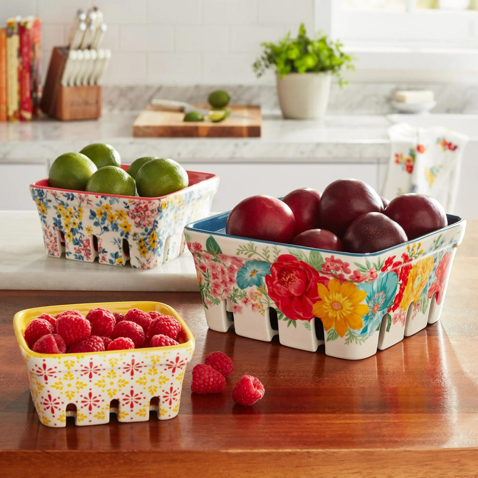 Three ceramic baskets filled with limes, plums, and raspberries respectively, displayed on a kitchen counter, suitable for decorative storage or serving