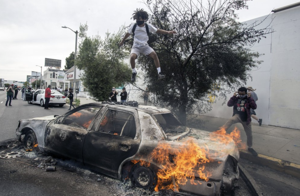 Pictured is a man jumping on a burning police car in LA. Source: AP