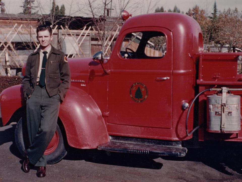 Richard Mirelles, a former forester, leaning against a red fire truck.