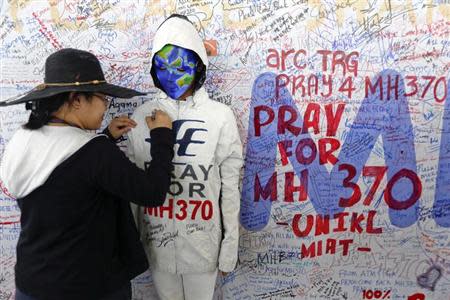 A woman adds her message on the clothes of a model during an art performance in support of the passengers of the missing Malaysia Airlines MH370 at the departure hall of Kuala Lumpur International Airport March 17, 2014. REUTERS/Damir Sagolj