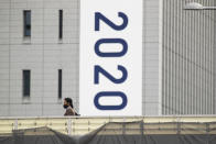 People wearing face masks walk on a crossover bridge near a banner to promote the rescheduled Tokyo 2020 Olympic Games in Tokyo Friday, April 2, 2021. Many preparations are still up in the air as organizers try to figure out how to hold the postponed games in the middle of a pandemic. (AP Photo/Hiro Komae)